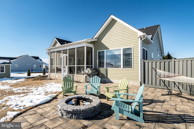 snow covered back of property with a patio area, a sunroom, and a fire pit