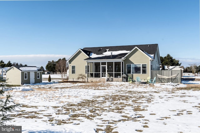 snow covered back of property with an outdoor structure and a sunroom