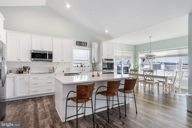 kitchen featuring decorative light fixtures, backsplash, a kitchen island, appliances with stainless steel finishes, and white cabinets