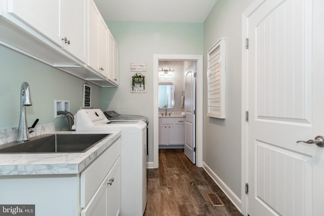 clothes washing area featuring cabinets, sink, washer and clothes dryer, and dark hardwood / wood-style floors