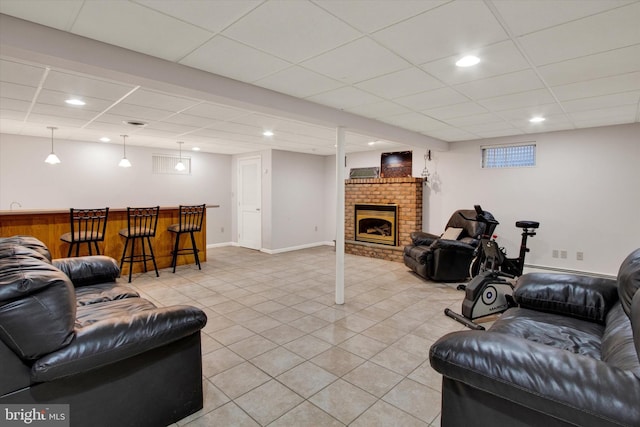 living room with a drop ceiling, light tile patterned floors, a fireplace, and indoor bar