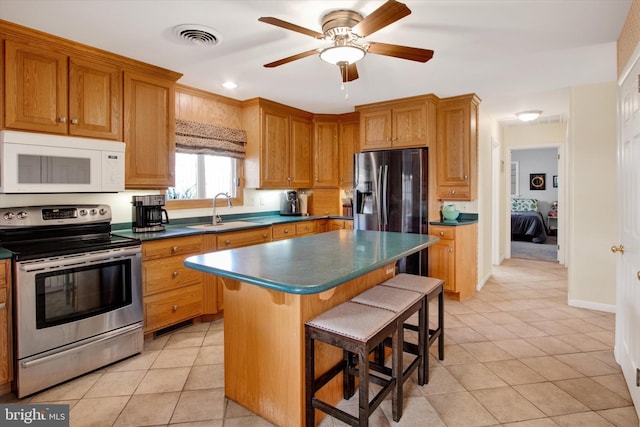 kitchen with light tile patterned flooring, a kitchen bar, sink, a center island, and appliances with stainless steel finishes