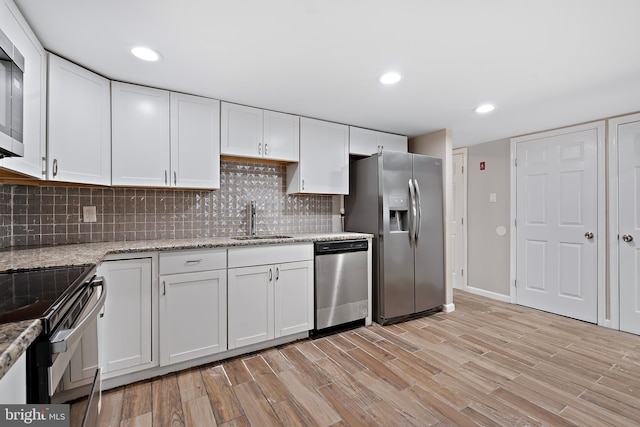 kitchen with sink, light stone countertops, light wood-type flooring, white cabinetry, and stainless steel appliances