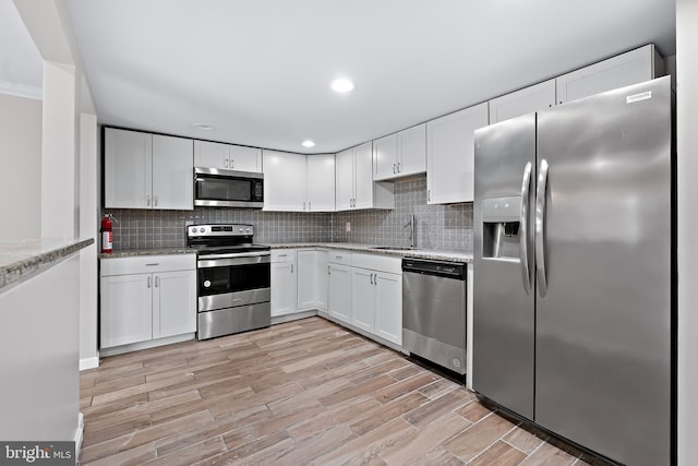 kitchen featuring sink, light stone counters, light hardwood / wood-style floors, white cabinets, and appliances with stainless steel finishes