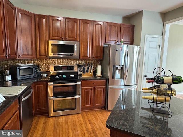 kitchen with stainless steel appliances, light hardwood / wood-style floors, dark stone countertops, and decorative backsplash