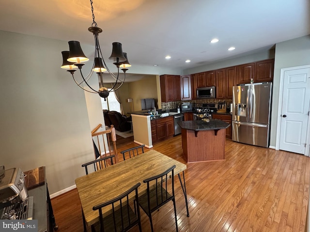 kitchen featuring light hardwood / wood-style flooring, a chandelier, decorative light fixtures, stainless steel appliances, and backsplash