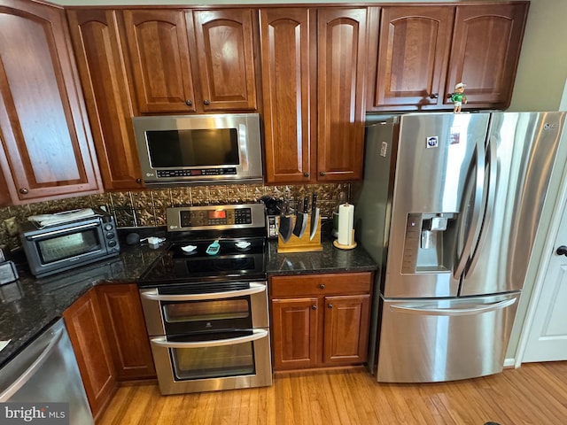 kitchen with appliances with stainless steel finishes, dark stone countertops, light hardwood / wood-style flooring, and tasteful backsplash