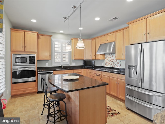 kitchen with appliances with stainless steel finishes, light brown cabinetry, a kitchen island, sink, and decorative light fixtures