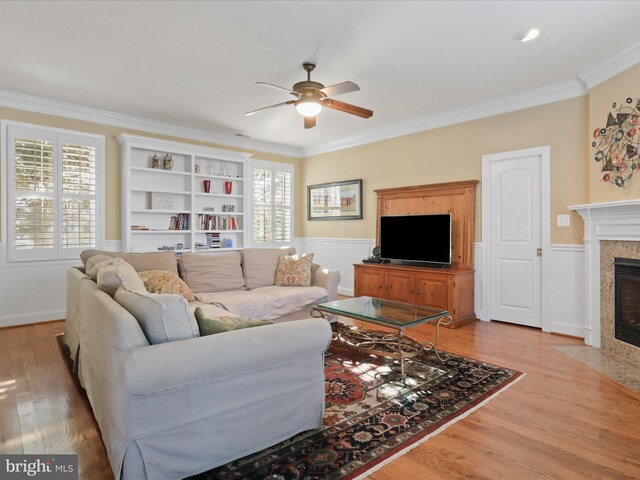 living room with a tile fireplace, ornamental molding, and ceiling fan