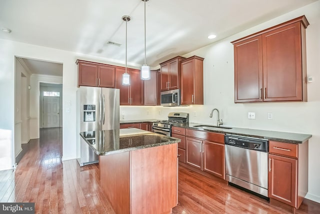 kitchen featuring dark stone counters, stainless steel appliances, sink, a center island, and hanging light fixtures