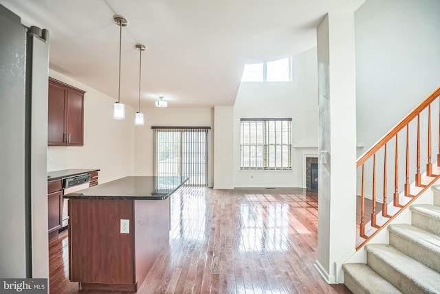 kitchen with dishwasher, a center island, wood-type flooring, decorative light fixtures, and a tiled fireplace