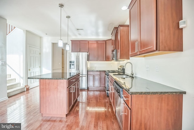 kitchen with a center island, sink, light wood-type flooring, appliances with stainless steel finishes, and decorative light fixtures