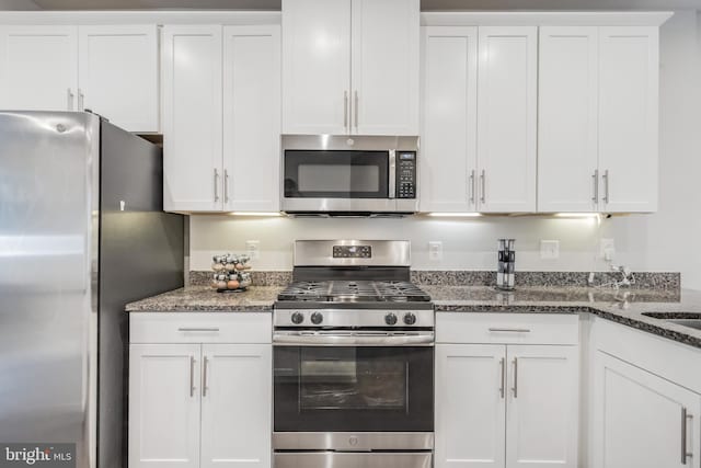 kitchen with dark stone countertops, stainless steel appliances, and white cabinets