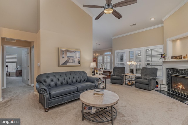 carpeted living room featuring a high end fireplace, crown molding, ceiling fan with notable chandelier, and a high ceiling