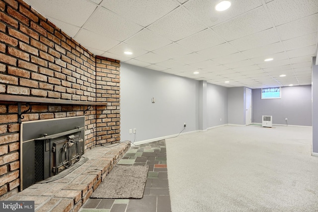 basement featuring carpet floors, a drop ceiling, and a wood stove