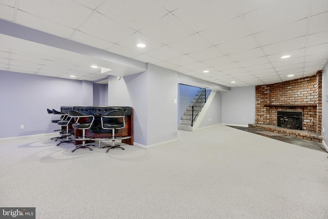 interior space featuring carpet, a drop ceiling, and a brick fireplace