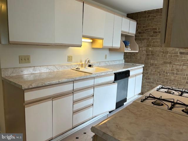 kitchen featuring light countertops, stainless steel dishwasher, a sink, and white cabinetry