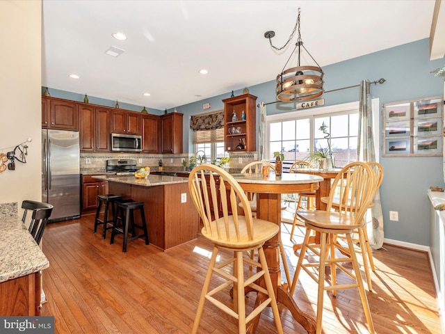 kitchen featuring appliances with stainless steel finishes, backsplash, light stone counters, decorative light fixtures, and light wood-type flooring