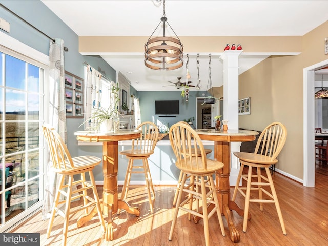 dining space with decorative columns, ceiling fan, and light hardwood / wood-style flooring