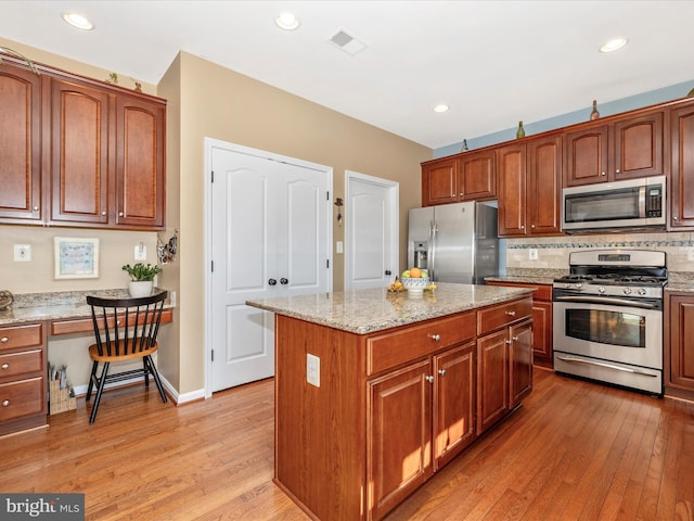 kitchen featuring a kitchen island, appliances with stainless steel finishes, built in desk, light stone counters, and light hardwood / wood-style flooring