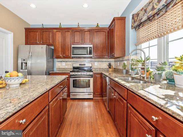 kitchen featuring appliances with stainless steel finishes, sink, backsplash, light stone counters, and light wood-type flooring