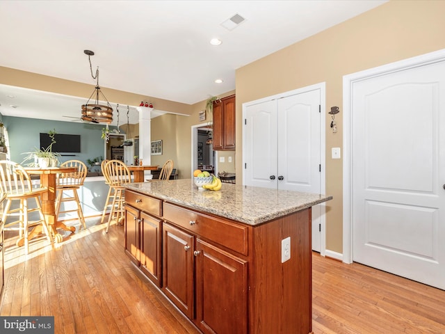 kitchen featuring light stone countertops, hanging light fixtures, a kitchen island, and light wood-type flooring