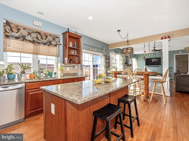 kitchen featuring sink, a center island, stainless steel dishwasher, light stone counters, and light hardwood / wood-style flooring