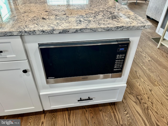 interior details featuring white cabinetry, light stone counters, and light hardwood / wood-style flooring