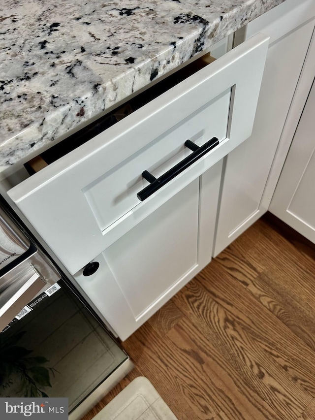 room details with hardwood / wood-style floors, white cabinets, and light stone counters