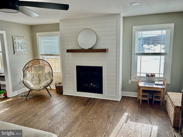 sitting room featuring ceiling fan, a large fireplace, a healthy amount of sunlight, and dark hardwood / wood-style floors