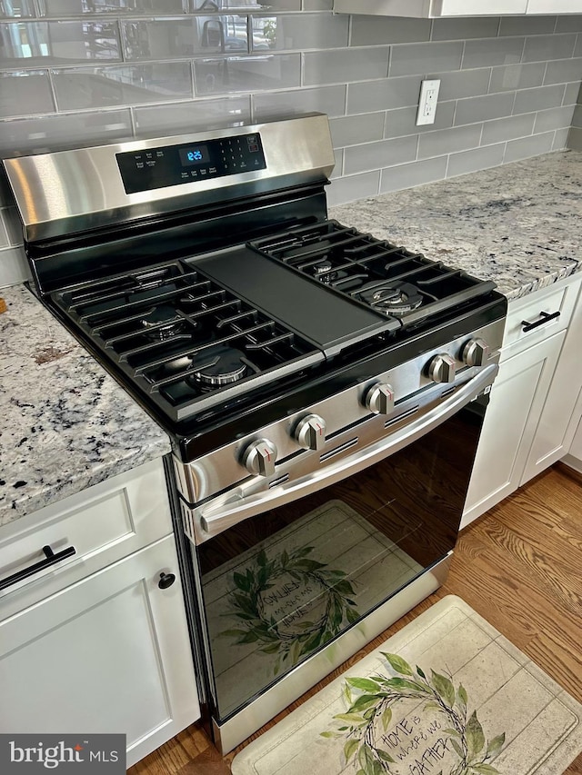 kitchen with light hardwood / wood-style flooring, white cabinetry, backsplash, stainless steel gas range oven, and light stone countertops