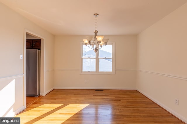 spare room featuring an inviting chandelier and hardwood / wood-style floors