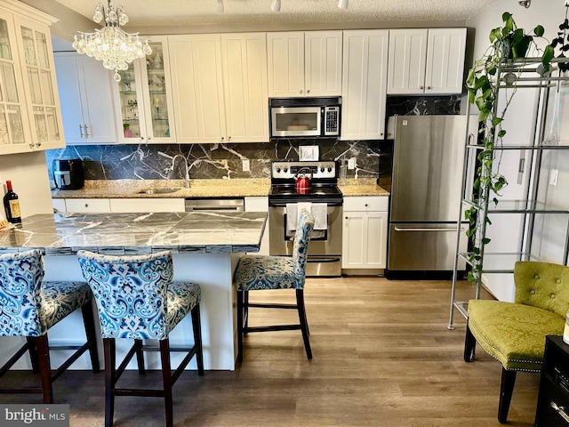 kitchen with appliances with stainless steel finishes, a kitchen bar, white cabinetry, and sink