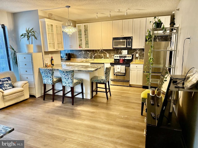 kitchen with white cabinetry, stainless steel appliances, a kitchen breakfast bar, hanging light fixtures, and light stone countertops