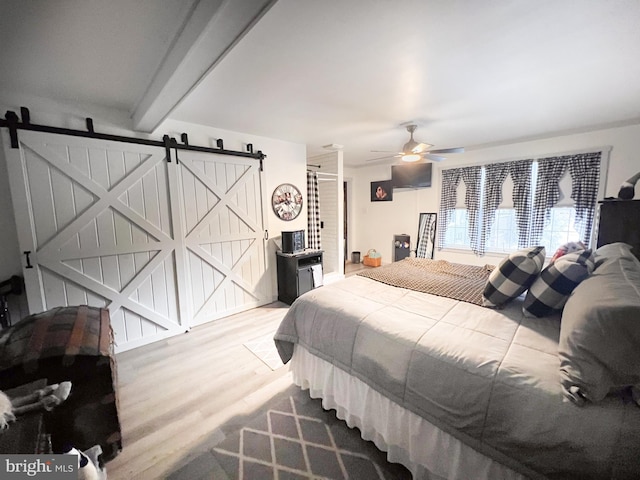 bedroom with beam ceiling, a barn door, ceiling fan, and hardwood / wood-style floors