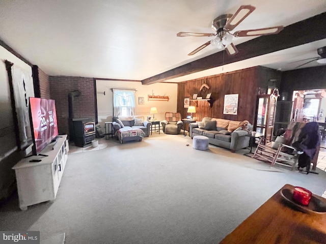 living room featuring beamed ceiling, a wood stove, ceiling fan, and wooden walls