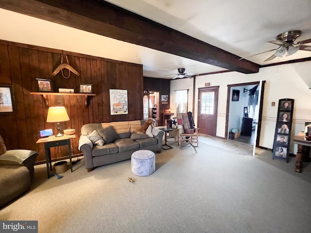 carpeted living room featuring beam ceiling, wood walls, and ceiling fan