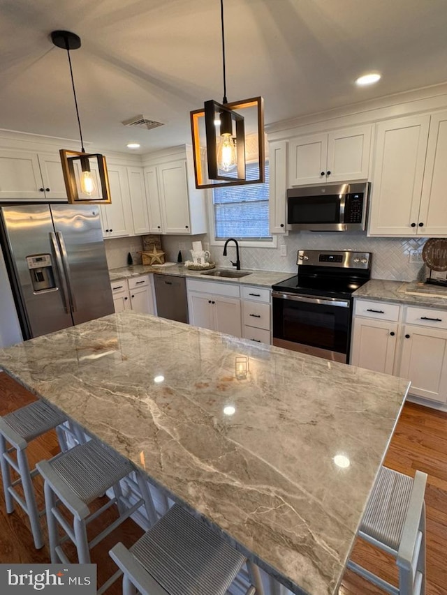 kitchen with white cabinets, stainless steel appliances, hanging light fixtures, a kitchen bar, and sink