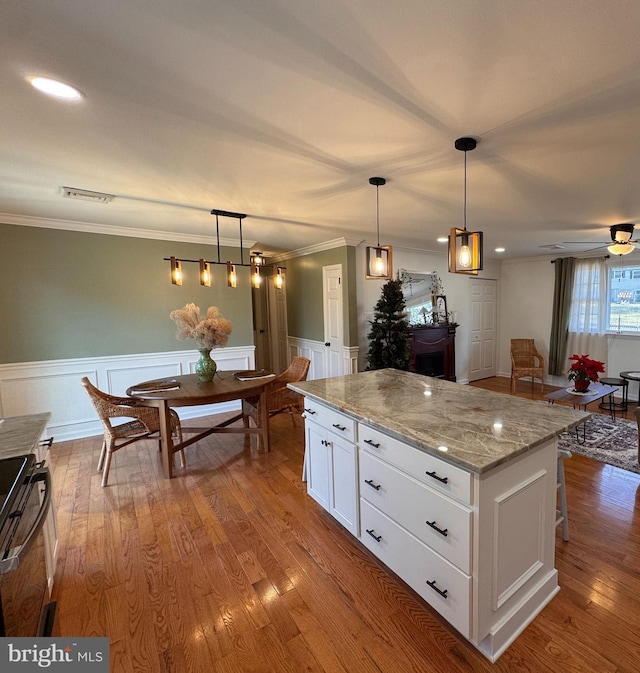 kitchen with white cabinetry, a center island, light stone counters, range, and hanging light fixtures