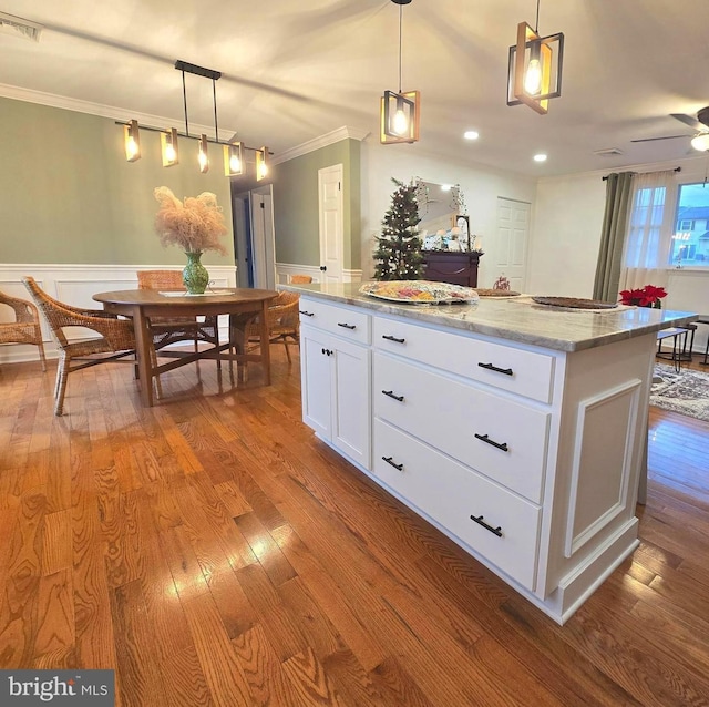 kitchen featuring light stone counters, white cabinets, decorative light fixtures, and a center island