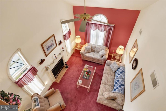 living room featuring a tile fireplace, ceiling fan, carpet, and a high ceiling