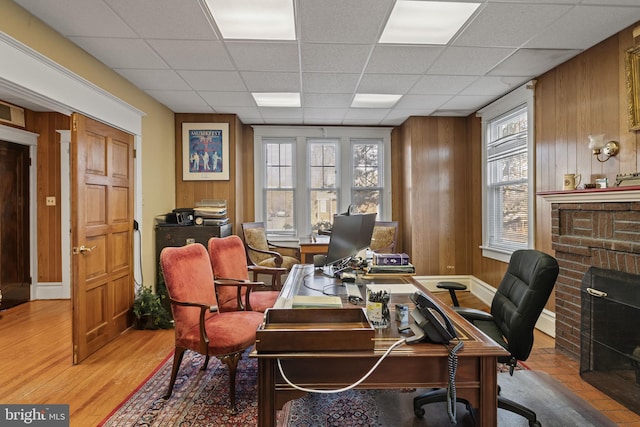 office space featuring a paneled ceiling, a brick fireplace, and wooden walls