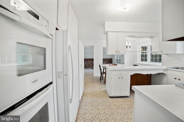 kitchen with backsplash, white appliances, white cabinets, and an inviting chandelier