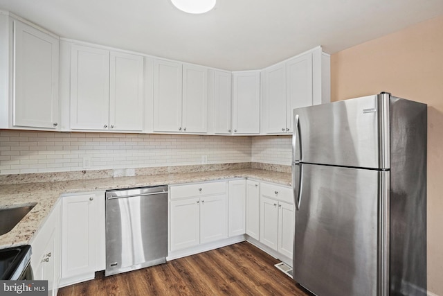 kitchen with appliances with stainless steel finishes, dark hardwood / wood-style flooring, white cabinetry, and light stone counters