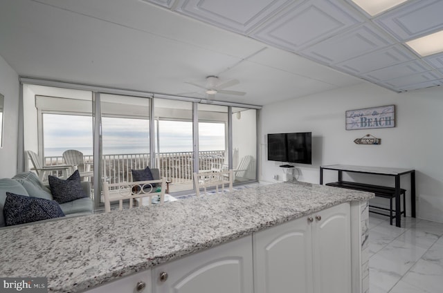 kitchen with ceiling fan, white cabinetry, floor to ceiling windows, and light stone counters