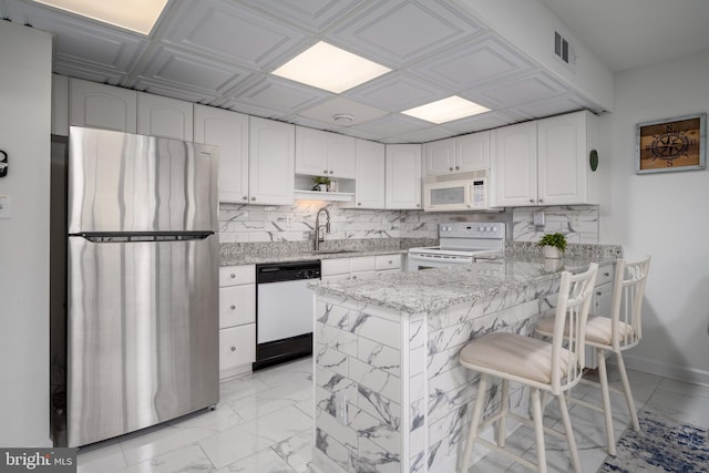 kitchen with light stone countertops, a kitchen bar, white cabinets, and white appliances