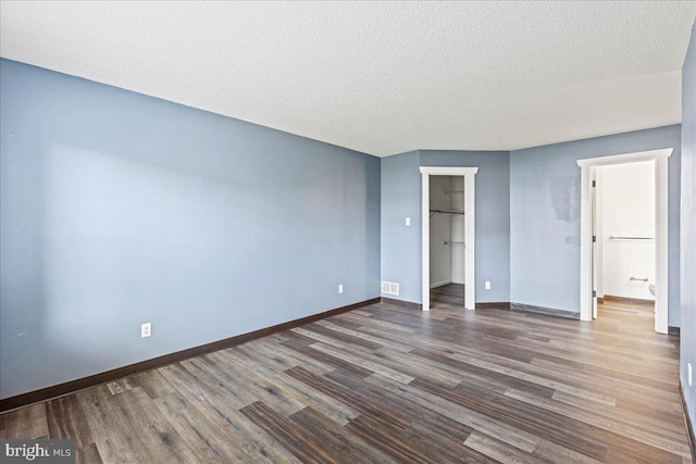 unfurnished bedroom featuring a textured ceiling, a walk in closet, a closet, and dark hardwood / wood-style floors