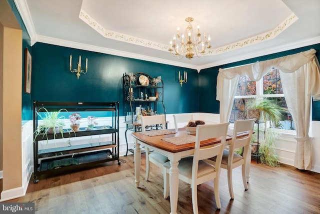 dining area with wood-type flooring, a tray ceiling, and a notable chandelier