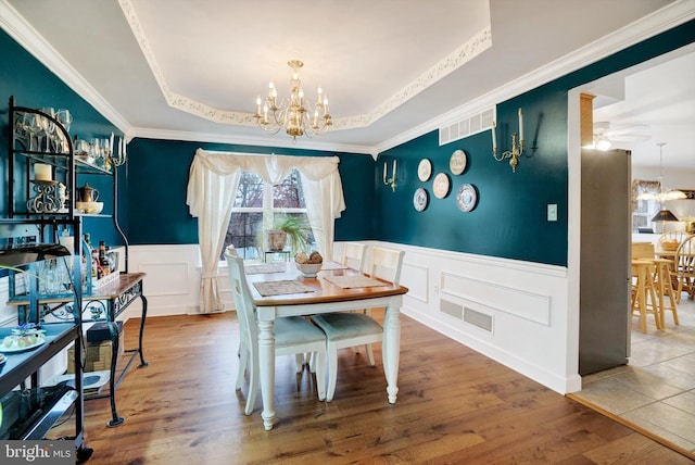 dining room with crown molding, ceiling fan with notable chandelier, hardwood / wood-style flooring, and a tray ceiling