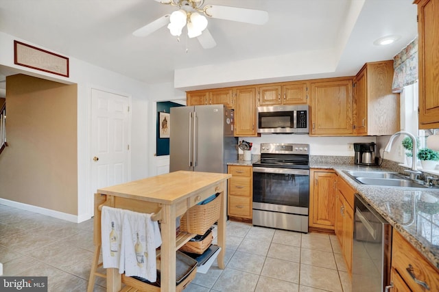 kitchen with light tile patterned floors, ceiling fan, appliances with stainless steel finishes, light stone counters, and sink